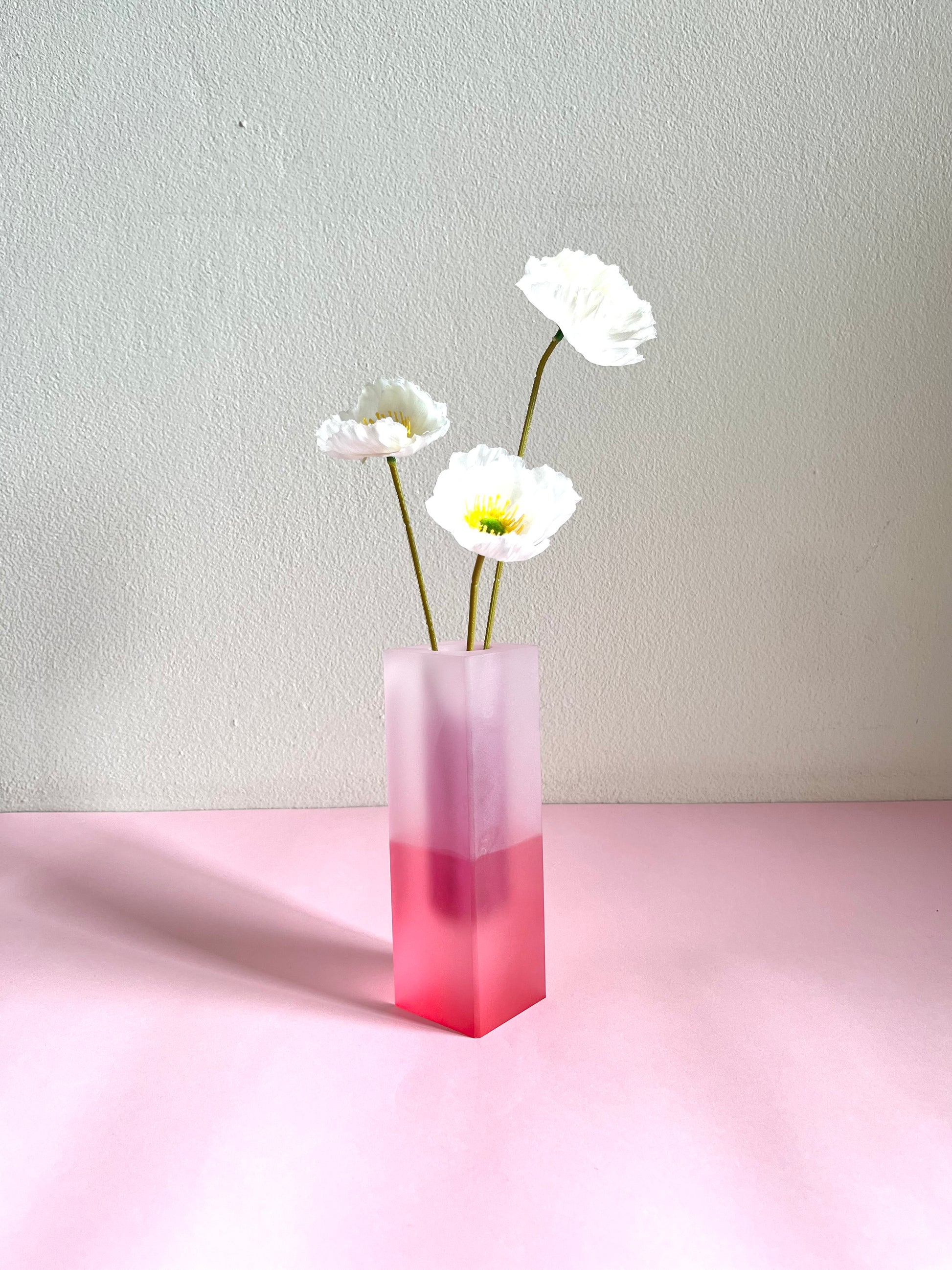 Pink gradient vase with white flowers on a light pink surface